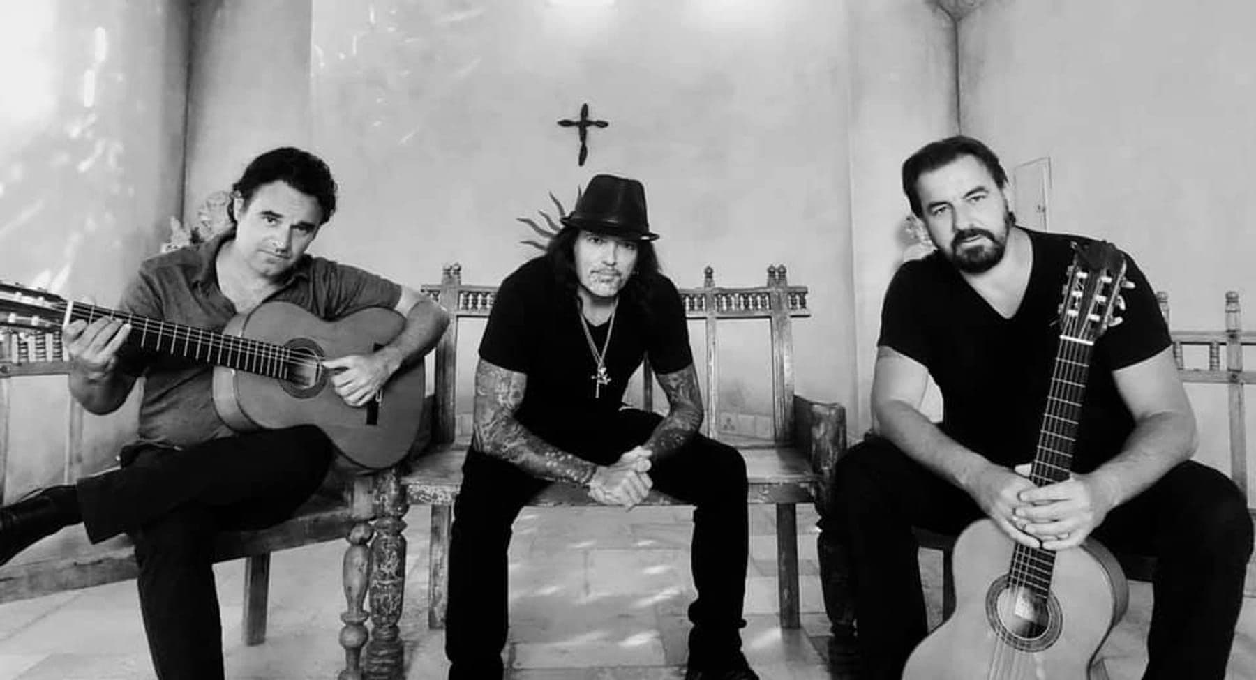 Calé — the trio seated with guitars against a plaster chapel wall